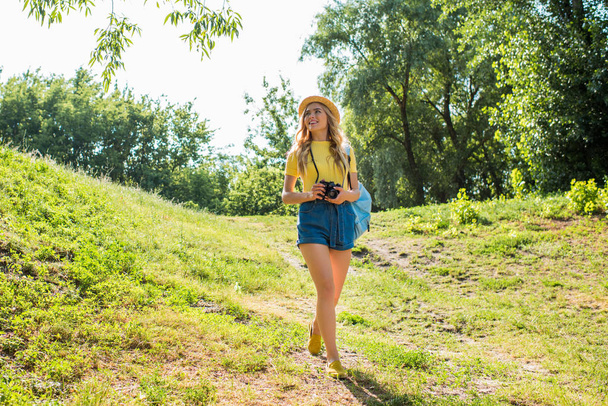 genç gülümseyen kadın yaz Park'ta yürüyordunuz fotoğraf makinesi ile şapkalı - Fotoğraf, Görsel