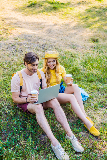 young couple with coffee to go using laptop in park - 写真・画像