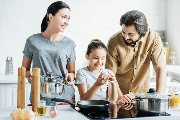 smiling family with little daughter cooking omelet at kitchen - Zdjęcie, obraz
