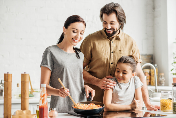 hermosa familia con pequeña hija cocinando tortilla en la cocina
 - Foto, Imagen