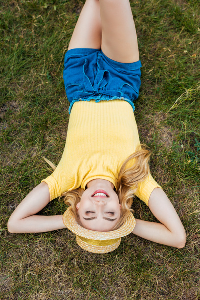 mosolygó fiatal nő kalapban pihenő Park zöld füvön felülnézete - Fotó, kép