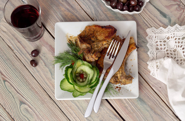 Duże kawałki mięsa wieprzowego na biały talerz z warzywami zbliżenie na drewnianym stole. - Zdjęcie, obraz