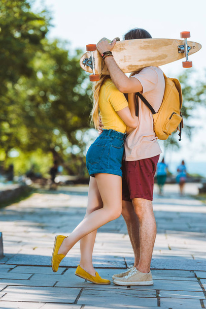 obscured view of couple kissing behind longboard in hands - Foto, Imagem