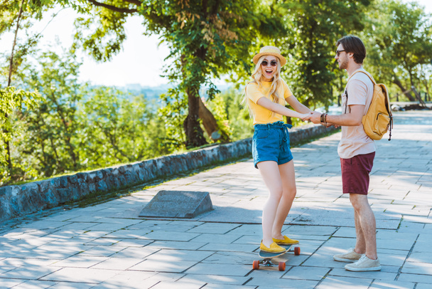 hombre ayudando novia patinaje en longboard en la calle
 - Foto, Imagen