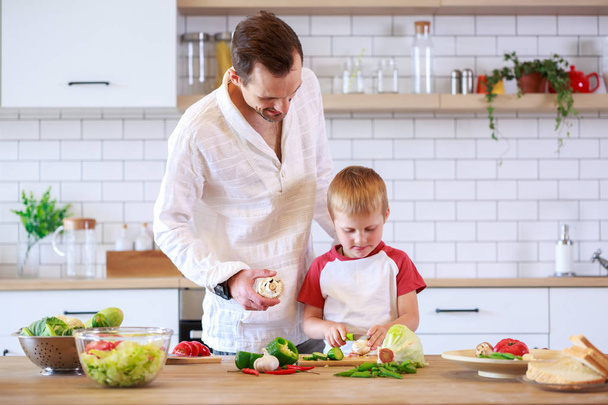 Photo of young father and son cooking at table with vegetables - Фото, зображення