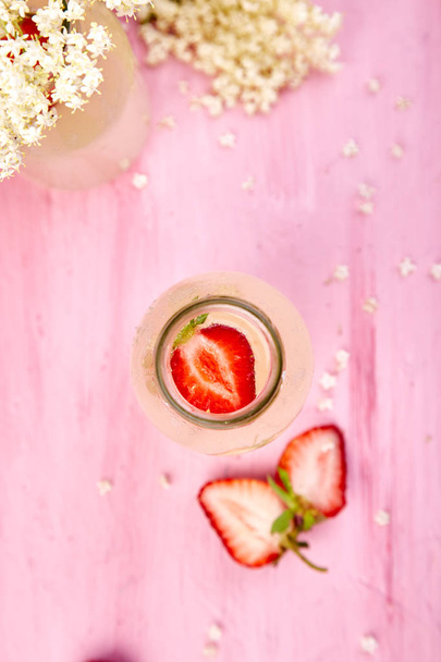 Kombucha tea with elderflower flower and strawberry on pink background. Homemade fermented infused drink. Summer Healthy natural probiotic flavored drink. Copy space. Top view. - Photo, Image
