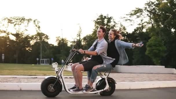 Young man and her girlfriend are riding an electric bile in the crowdy green park. Wearing casual. Happy moments, enjoying life - Filmagem, Vídeo