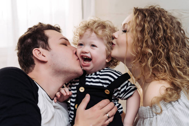 familia alegre amistosa, padres jóvenes, padre y madre abrazan a su pequeño hijo de pelo rizado
 - Foto, imagen