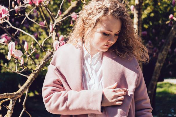 curly young woman in a pink coat enjoying a holiday in a spring park in the sun - Photo, image