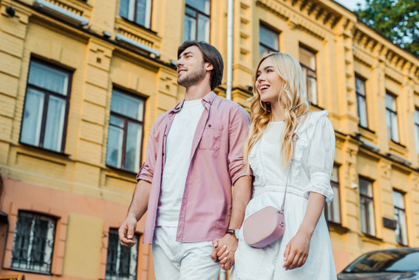 young couple holding hands while walking on city street together - Fotografie, Obrázek