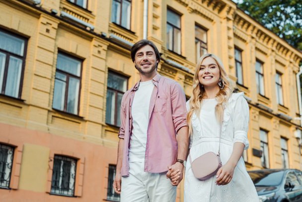 young couple holding hands while walking on city street together - Zdjęcie, obraz