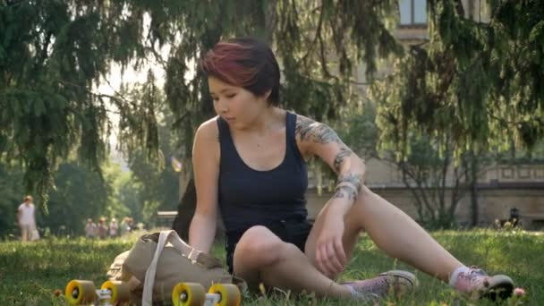 Ασιατικές νεαρές γυναίκες με τατουάζ μόνιμη από γρασίδι και πηγαίνουν στο Πανεπιστήμιο, κρατώντας σακίδιο και skateboard - Πλάνα, βίντεο