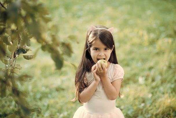 Food, diet, vitamin. Little girl eat apple on natural background, vitamin - Foto, afbeelding