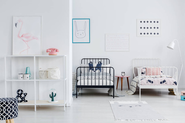Siblings room interior with modern style metal beds, one white, the other black, Posters on a white wall. Cupboard with minimal decorations. Real photo. - Zdjęcie, obraz