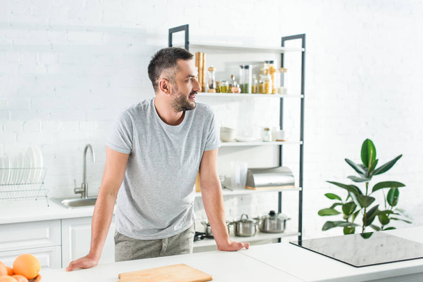side view of smiling man standing near table on kitchen  - Foto, Imagen