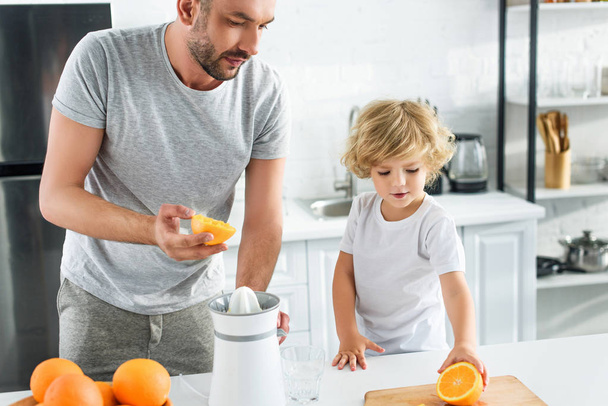 キッチンで新鮮なジュースを作るためオレンジ色の父を与える少年  - 写真・画像
