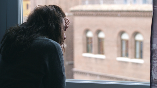 mujer triste deprimida apoyada contra la ventana. Desesperación, angustia
 - Imágenes, Vídeo