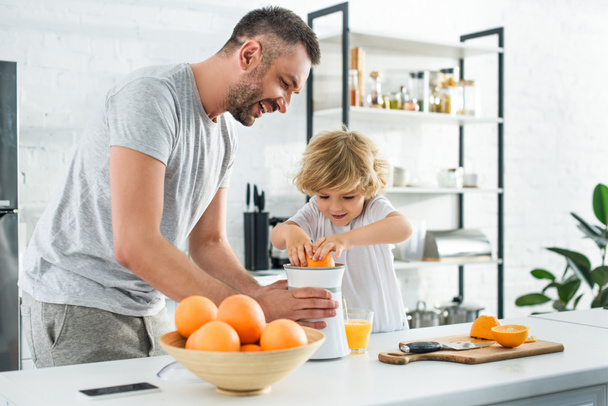 笑顔の父と幼い息子の調理道具で、台所のテーブルの上で新鮮なオレンジ ジュースを作る  - 写真・画像