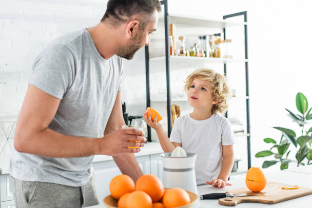 son and father looking at each other after making fresh orange juice at kithen - Φωτογραφία, εικόνα