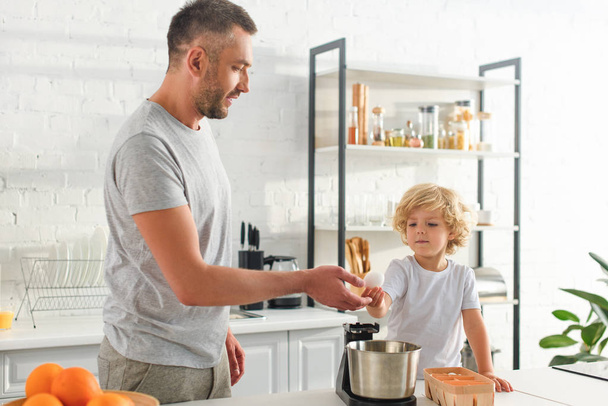 boy giving egg to father near tabletop at kitchen  - Photo, Image