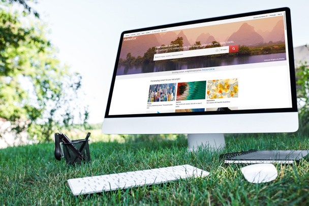 selective focus of textbook and computer with shutterstock website on grass outdoors  - Fotografie, Obrázek