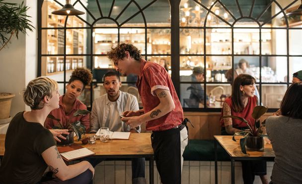 Genç garson emir birlikte bir Bistro bir masada oturan müşteriler bir grup gülümseyen - Fotoğraf, Görsel