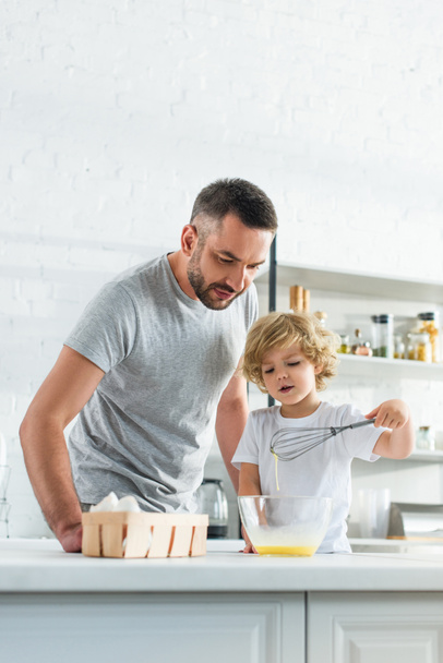 father with son whisking eggs in bowl at kitchen  - Photo, Image