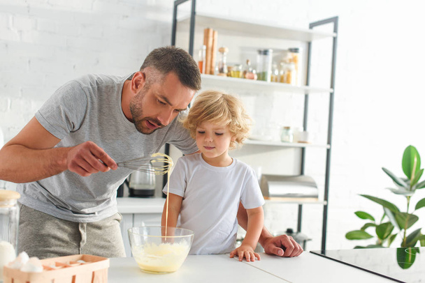 man teaching son making dough in bowl at kitchen - Foto, afbeelding