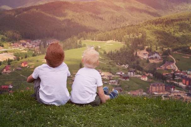 Δύο αγόρια κάθεται πάνω σε ένα λόφο και βλέπουν τα βουνά. Πίσω όψη - Φωτογραφία, εικόνα