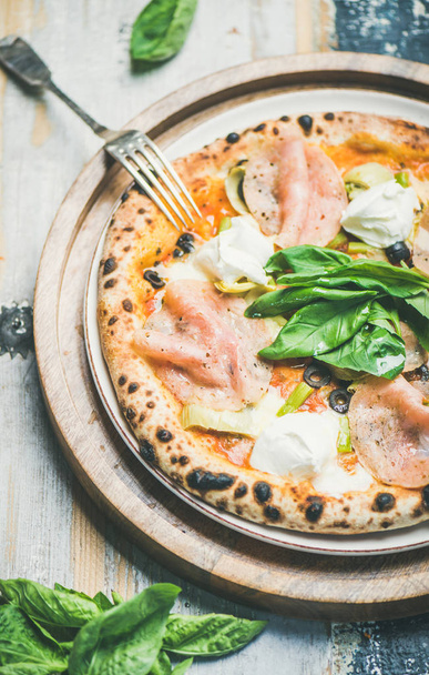 Freshly baked pizza with artichokes, smoked turkey ham, olives, cream cheese and basil over rustic wooden background - Foto, afbeelding