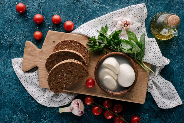 Wooden board with mozzarella and bread on dark blue table with red tomatoes - Photo, image