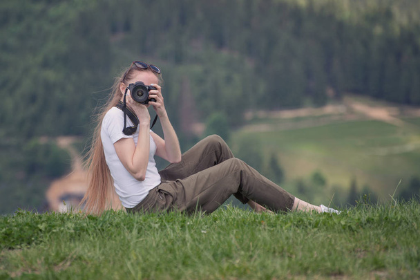 Meisje met de camera zit op een heuvel en foto's. Bos op de achtergrond - Foto, afbeelding