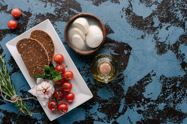 Teller mit Tomaten und Brot auf dunkelblauem Tisch mit Mozzarella und Öl - Foto, Bild