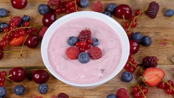Erdei gyümölcs joghurtot tálba forgatható az asztal tele friss gyümölcsökkel. Egészséges reggeli étkezési koncepció. 4k - Felvétel, videó