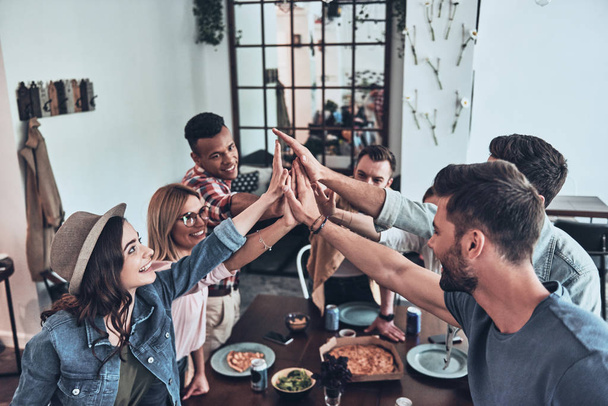happy friends giving each other high-five and smiling while having dinner party at table  - Photo, image