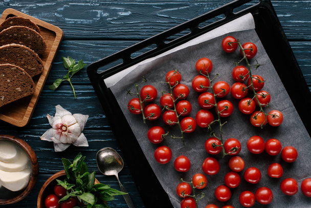 Red cherry tomatoes in baking on dark wooden table by condiments and bread - Φωτογραφία, εικόνα
