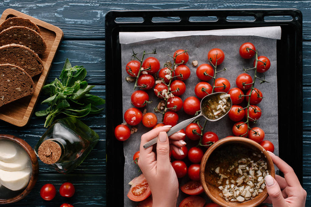 Cropped view of female hands pouring garlic oil on cherry tomatoes in baking pan - Foto, immagini