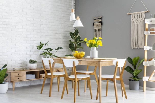 White lamps above wooden table and chairs in dining room interior with yellow flowers. Real photo - Photo, Image
