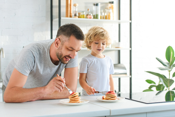 ευτυχής πατέρας και γιος τρώγοντας τηγανίτες στην κουζίνα  - Φωτογραφία, εικόνα