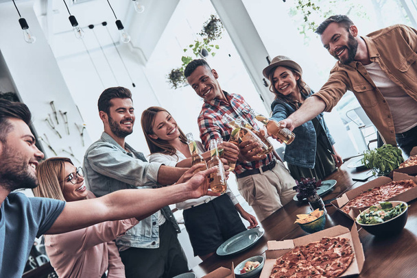 group of young people in casual wear toasting each other and smiling while having a dinner party - Foto, afbeelding