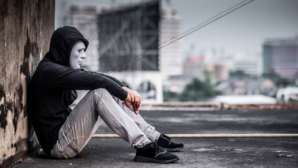 Ο άνθρωπος μυστήριο σε λευκή μάσκα με ζακέτα, κάθεται σκέφτεται κάτι με τα λυπημένα μάτια. κατάθλιψη μόνη καταστροφή αυτοκτονίας τοξικομανών ναρκωτικών έννοια - Φωτογραφία, εικόνα