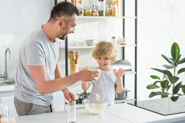 laughing father and son having fun while making dough in bowl at kitchen - Foto, Imagem