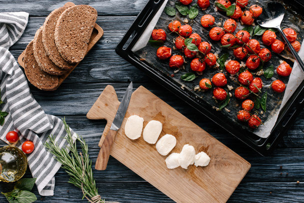 Pieces of bread and mozzarella on dark wooden table with tomatoes in baking pan - Foto, imagen
