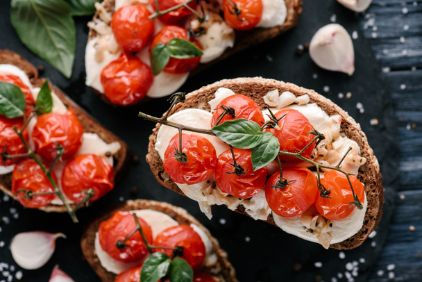 Delicious sandwiches with mozzarella and baked tomatoes on dark wooden table - Photo, Image