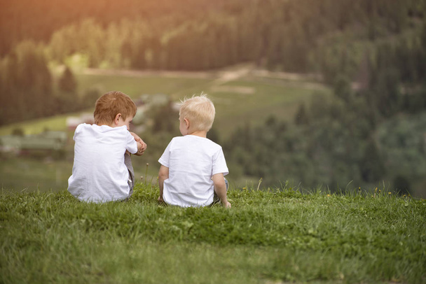 Δύο αγόρια κάθονται στο λόφο και μιλάμε χαρωπά. Πίσω όψη - Φωτογραφία, εικόνα
