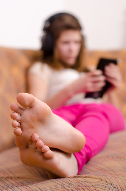 Linda chica adolescente que se divierte con la tableta PC mientras está acostado en el sofá. El foco está en los pies
 - Foto, imagen