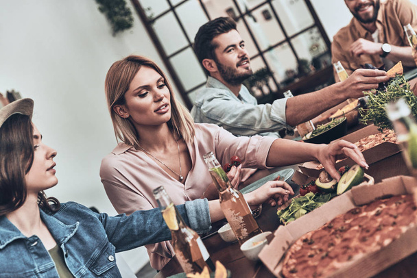 young people in casual clothing eating and smiling while having pizza - Foto, afbeelding