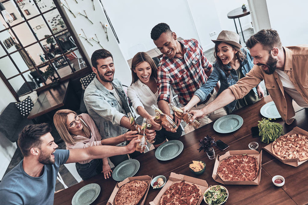 top view of young people in casual wear toasting each other and smiling while having a dinner party indoors - Foto, immagini