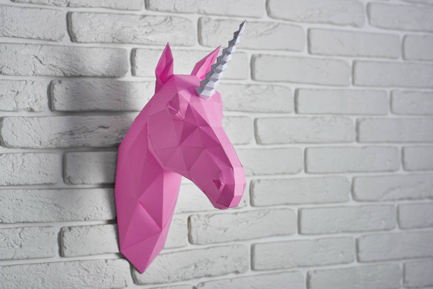 Bright pink unicorns head, made of paper hanging on white brick wall. - Foto, Imagem