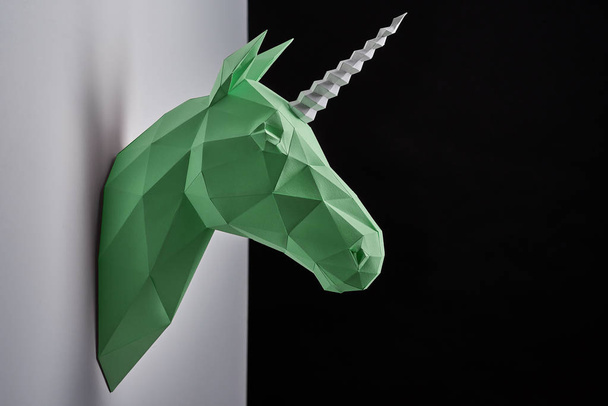 Horizontal shoot of green unicorns head hanging on grey shadowed wall. - Фото, изображение